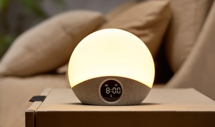 Luminous spherical device with digital display on a wooden surface, surrounded by pillows.